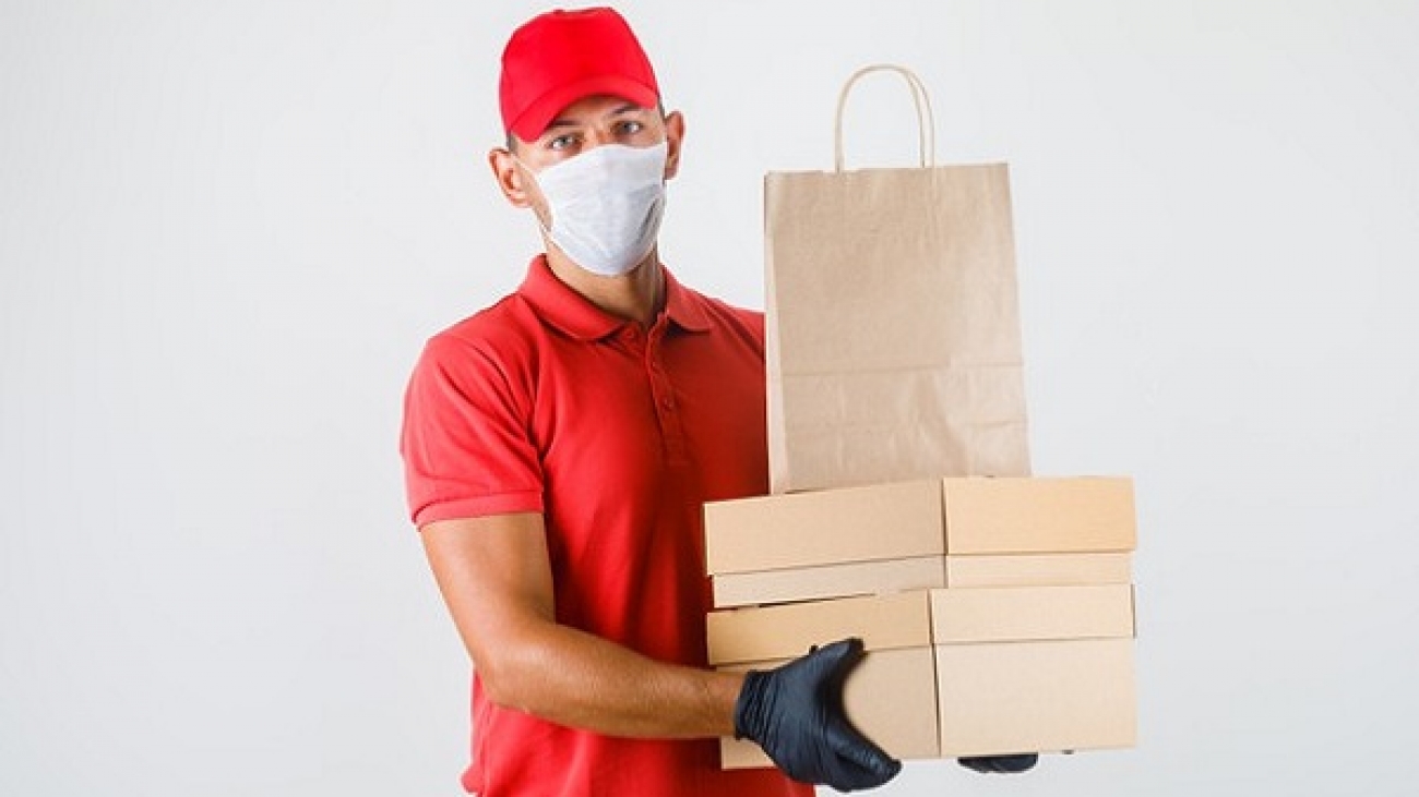 delivery-man-holding-cardboard-boxes-paper-bag-red-uniform-medical-mask-gloves-front-view_176474-10365